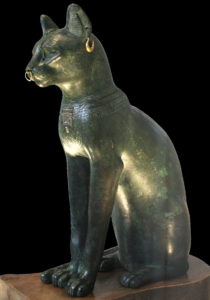 Sculpture en bronze de chat assis vu de profil, orné d'annaux dorés aux oreilles et au nez.